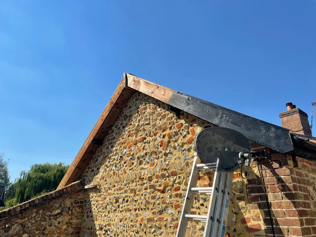 Fascia replacement in progress, new timber fitted alongside already-completed black-painted sections, listed property near Thetford